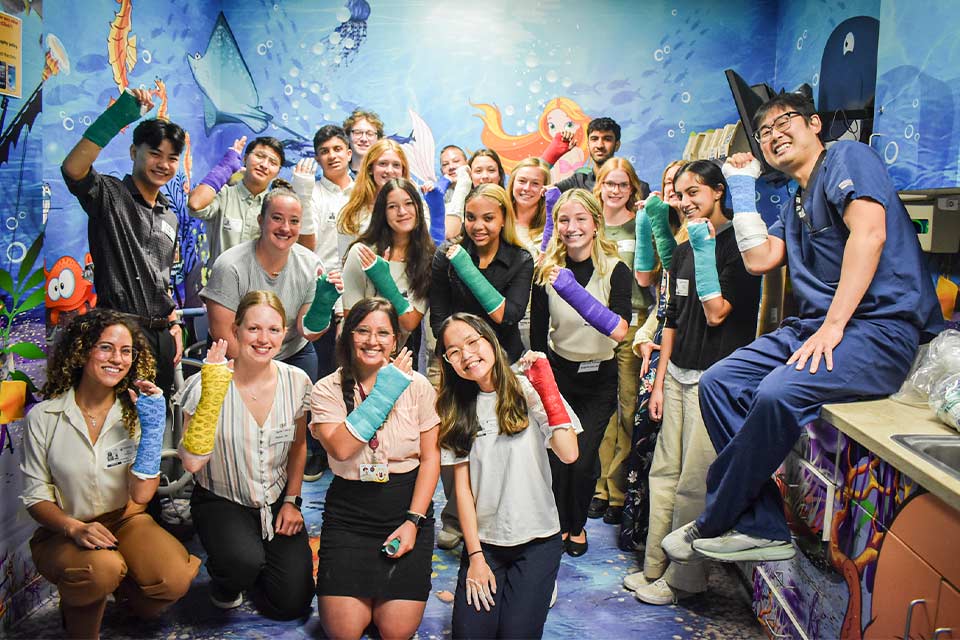 Students smiling and showing off their casts in an ocean-themed room.