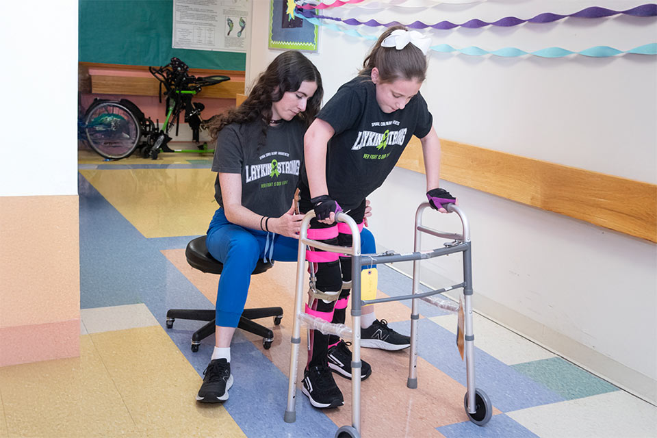 Laykin using a walker with the assistance of staff.