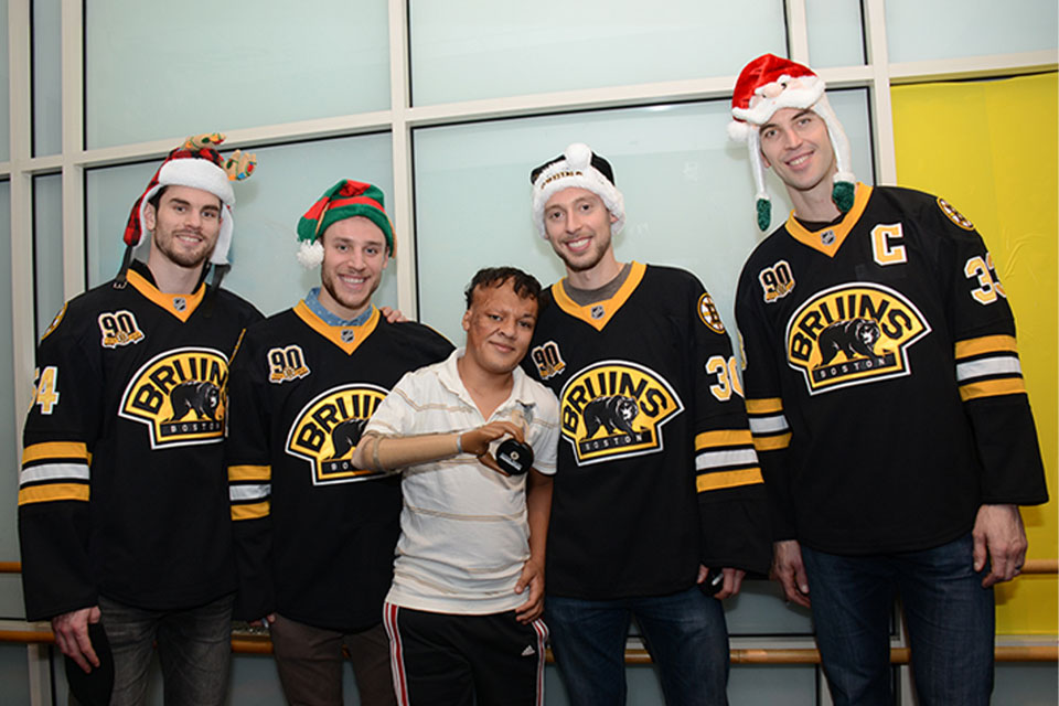 Josue, un paciente, sostiene un disco de hockey con cuatro miembros del equipo de hockey Boston Bruins.