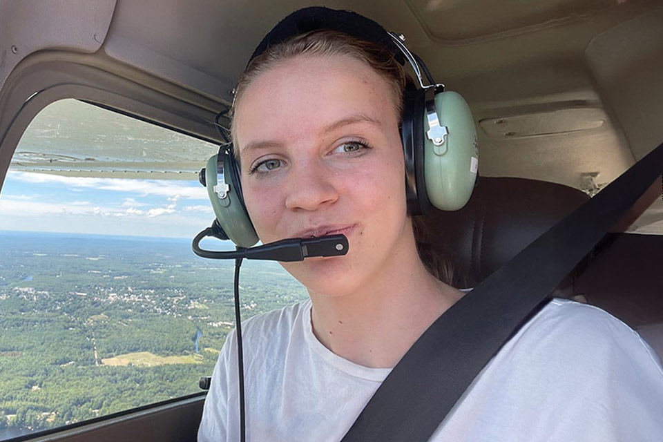 Female burn patient wearing a large headset with a microphone over her mouth in a small aircraft overlooking a forest